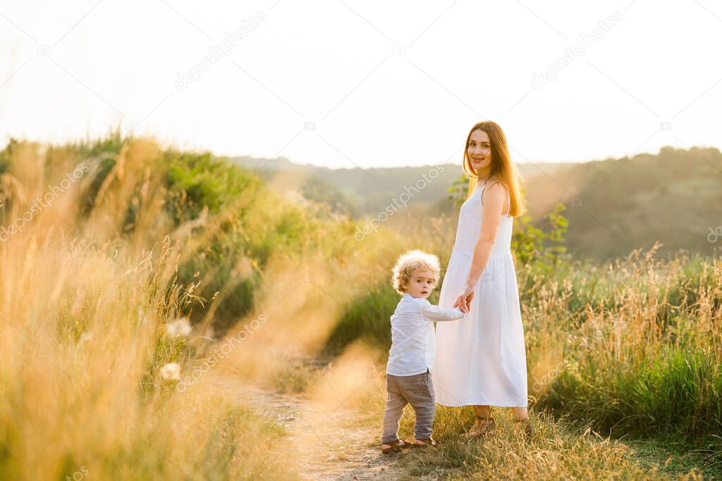 Happy mother and son are walking in picturesque field at sunset