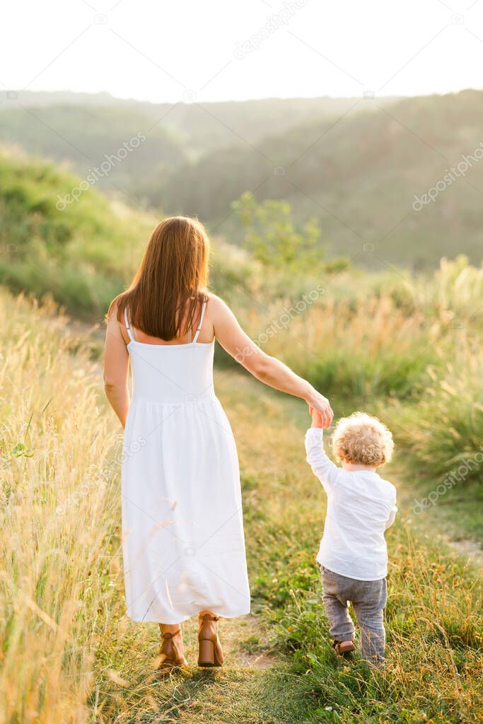 Happy mom with little son walk by the hand in nature