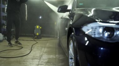 Yüksek basınçlı çamaşır makinesi olan bir araba tamircisi. Adam bir jet suyla arabayı duruluyor.