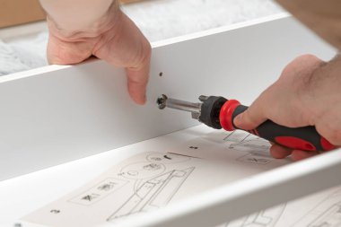 Adam ışık panosuna vida sokuyor. Yakın çekim tornavida elinde. Evde mobilya montajı