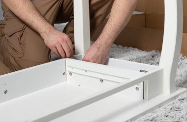 Adam evde beyaz tuvalet masası topluyor. Mobilya montaj konsepti