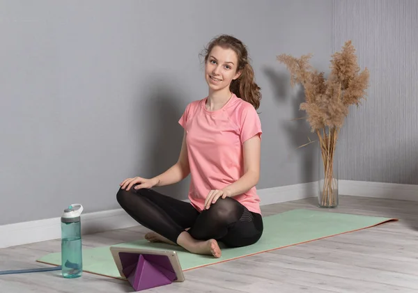 young woman on a gymnastic mat and waiting to start yoga class online