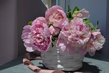 Masanın üzerinde beyaz bir sepet içinde pembe şakayık demeti. Zarif çiçek arkaplanı