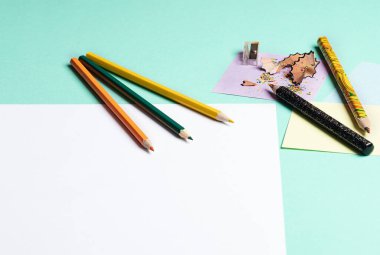 colored pencils and a sheet of white paper on a light green background. Back to school