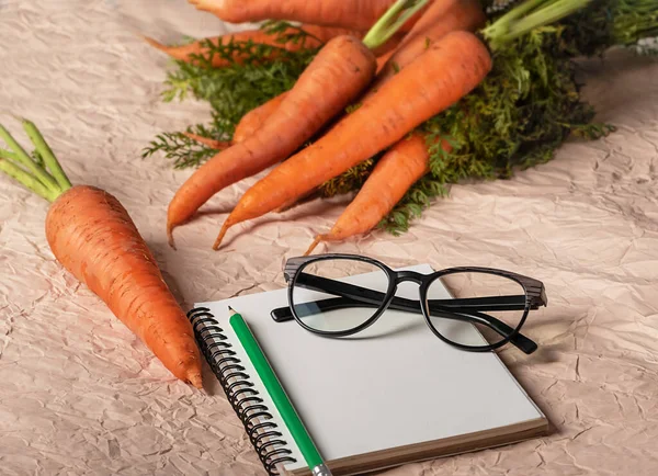 Havuç ve gözlük açık arkaplanda, defter ve yeşil kalemle.
