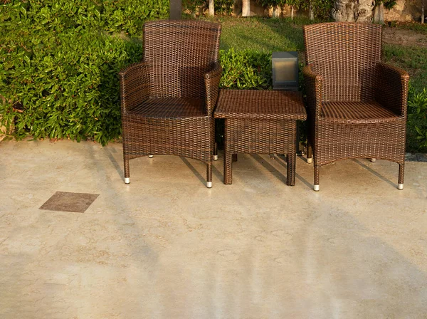 rattan furniture for relaxing in the park. Chairs and table on a background of green bushes