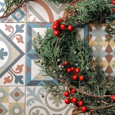 Yılbaşı çelengi, kırmızı böğürtlen ve altın rengeyiği retro geometrik fayanslarda. Nandian ağı, yeşil dal ve kırsal çam tacı. Düz yatıyordu. Noel konsepti. Yukarıdan.