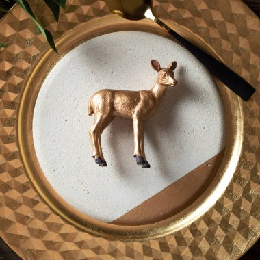 Tahta arka planda, doğal dallarla çevrili tabakta tatil yeri dekorasyonu ve oyuncak altın ren geyiği süslemesi..