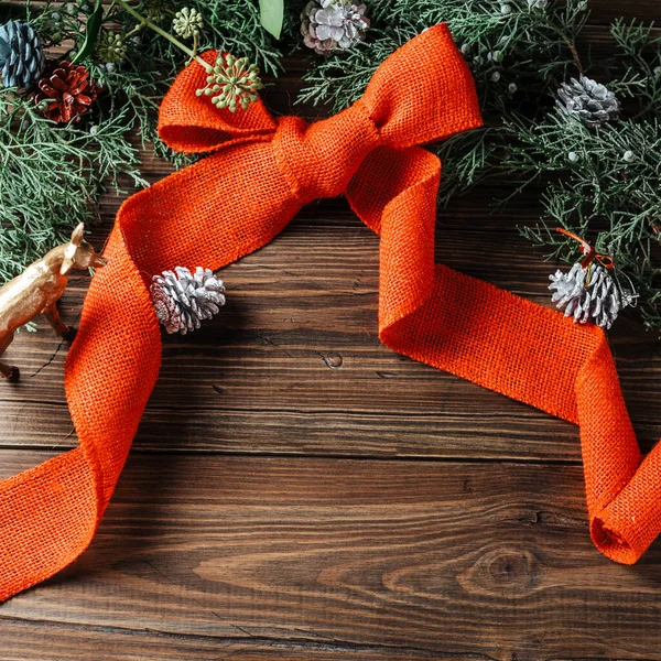 Noel ağacı dallarından yapılmış, ahşap arka planda kırmızı kurdeleyle süslenmiş yaratıcı bir düzen. Düz yatıyordu. Doğa Noel konsepti