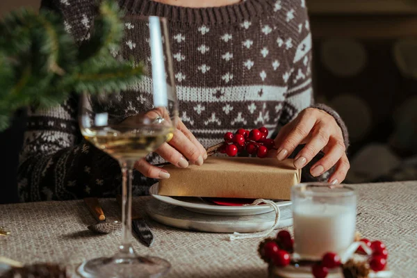 Kırmızı böğürtlenlerle süslenmiş bir Noel hediyesini açan kadın, evde yemek yerken el ele tutuşan aile Noel Kutlaması Konsepti.