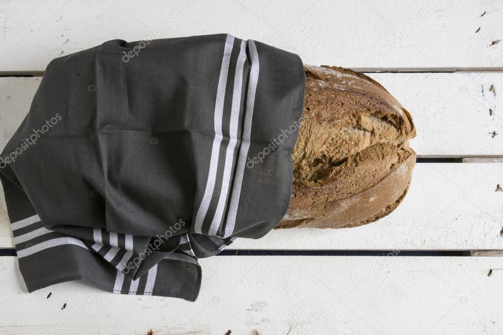 rustic bread, wrapped in striped fabric on white wooden backgrou