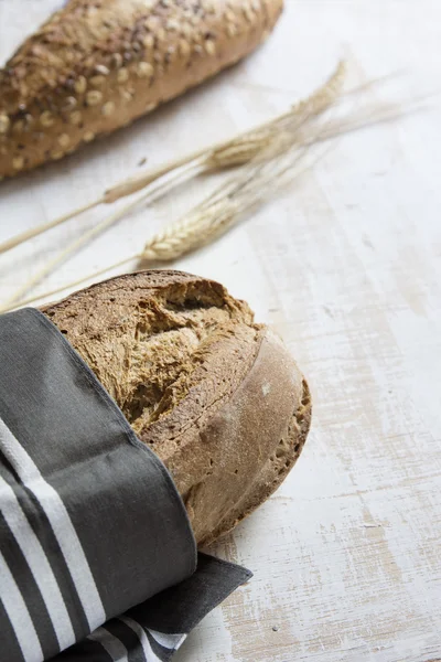 Rusztikus kenyér, csíkos szövet a fehér fa háttérb csomagolva — Stock Fotó