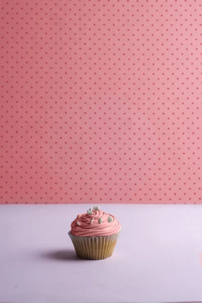 Roze cupcake met slagroom en hart hagelslag op gestippeld — Stockfoto