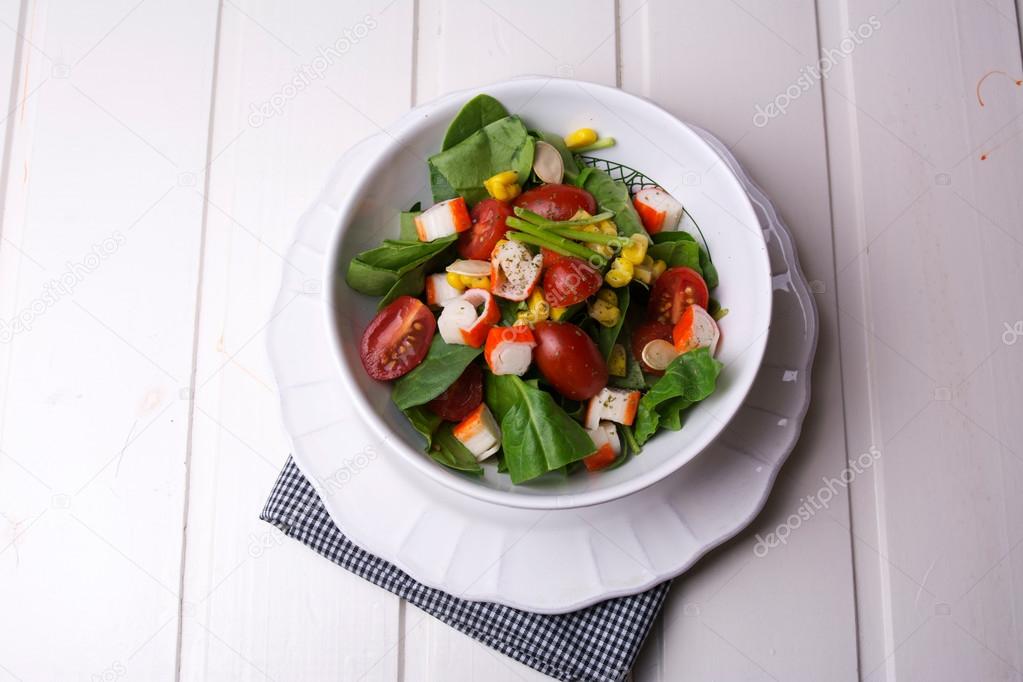 spinach salad with cherry tomatoes and corn in bowl, white woode