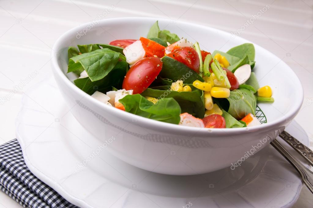 spinach salad with cherry tomatoes and corn in bowl, white woode