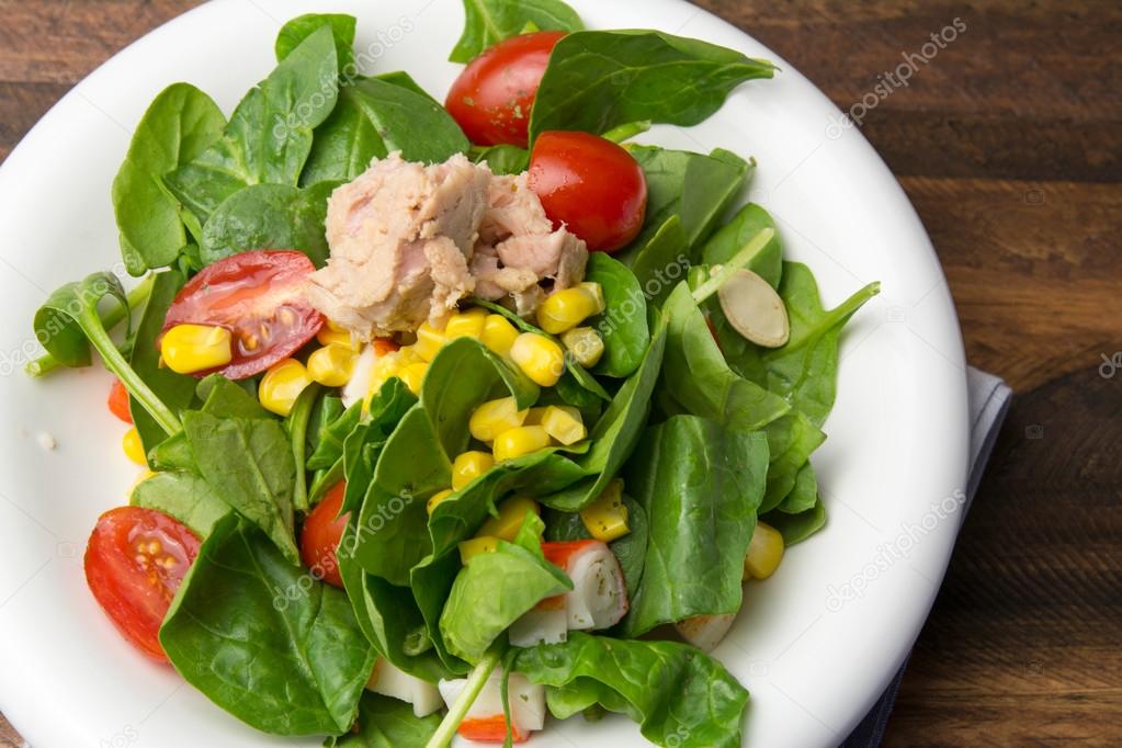 Fresh spinach salad with tuna and corn, small pieces of cherry t