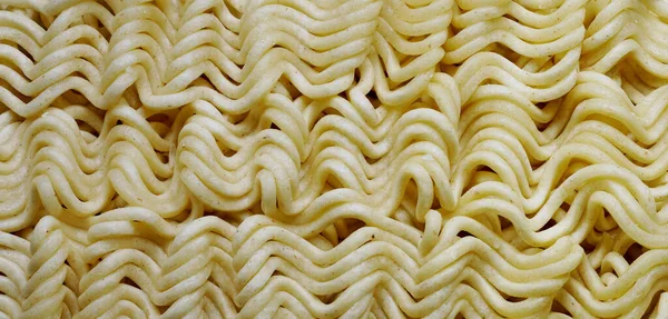 Instant noodles.Close up of raw dried noodles.Uncooked noodles texture.Precooked dehydratenoodleblocks.Asian food. Food background.Full depth of field. Panoramic image. Hi-res banner.