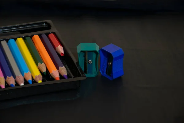 Picture of color pencil box and two pencil sharpener on black background.