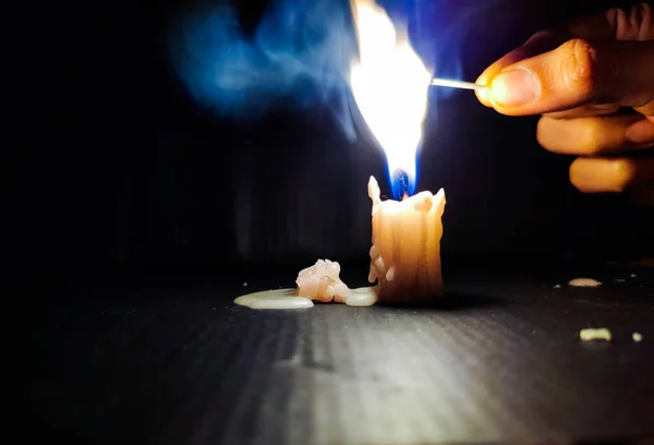 Stock photo of a human hand holding lighted matchsticks with yellow and blue color flame for lighting up the white color small candle on black dark background. focus on object.