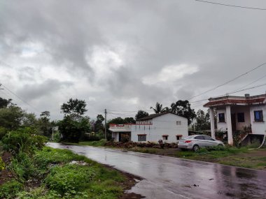 Kolhapur, Hindistan - 14 Ağustos 2021; Vahşi kırsalın çatısında kırmızı kiremitli beyaz renkli bungalovun stok fotoğrafı. Muson mevsiminde bungalovun dışında park edilmiş araçlar.