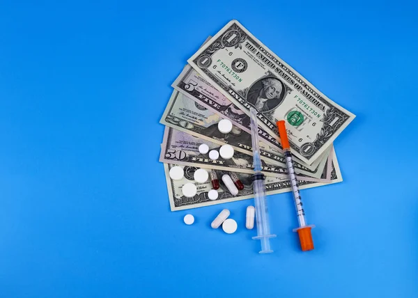 American dollars, a syringe, an insulin syringe, pills, capsules on a blue background. The concept of selling medicines, large price of medicine.