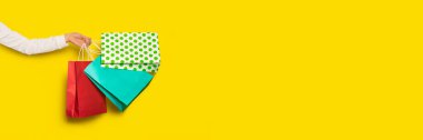 Alışveriş ya da satış konsepti. Kadın el, sarı arka planda izole edilmiş kağıt torbaları tutuyor. Kopyalama alanı olan uzun pankart.