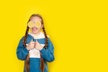 Gözlerini limonlu lolipopla kapatan kız çocuğu. Genç kız, sarıda izole edilmiş çubukta şeker tutuyor. Kopyalama alanı olan pankart