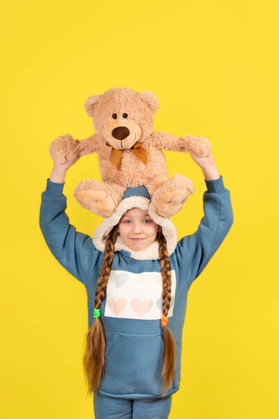 Девочка-подросток держит игрушечного плюшевого мишку. Девочка-подросток в современной одежде с длинными волосами играет с плюшевым мишкой.