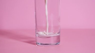 Pembe arka planda şeffaf bir bardağa organik süt dökülüyor. 4k çözünürlüklü yavaş çekim. Ev yapımı latte ya da milkshake için video eğitimi. Adım 1 - Süt dök.