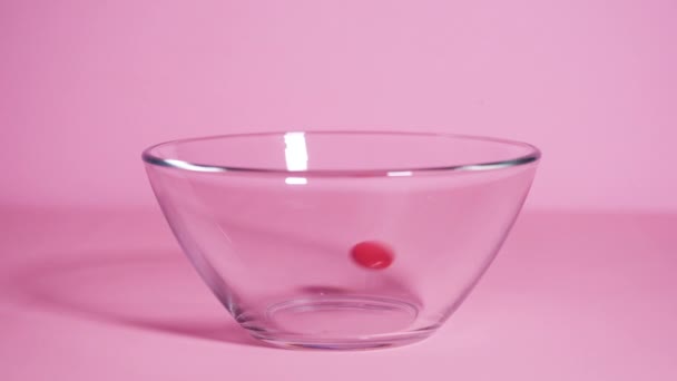 ピンクの背景にガラスのボウルに落ちるキャンディーの遅い動き スローモーションでカメラの前を通る多色のおいしいキャンディーボール — ストック動画