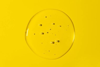 Şeffaf yuvarlak sıvı jel damlasını temizle ya da sarı arkaplanda izole edilmiş bir leke. Üst Manzara. Virüs koruması ya da kozmetik konsepti. Serum dokusu