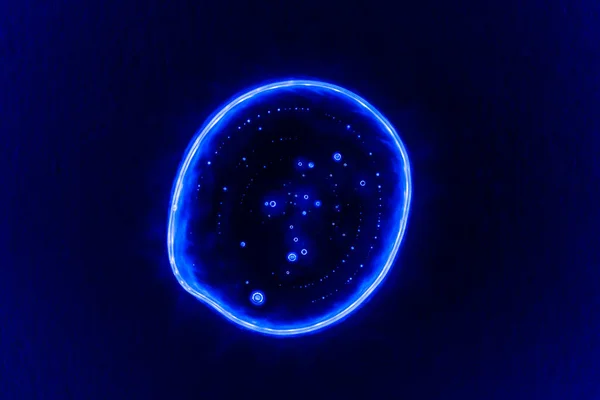 Clear transparent liquid gel dark blue drop or smear with neon light blue flare isolated on dark blue background. Top view. Virus protection or cosmetics concept. Serum texture.