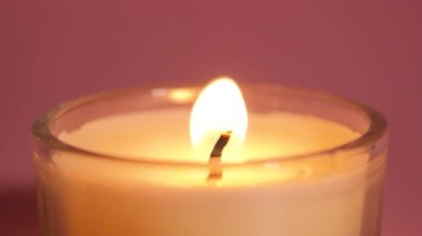 Pembe arka planda yanan mum. Mum alevinin yavaş çekim videosu yaklaş. Romantik ve rahatlatıcı bir kavram.