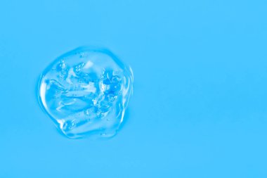 Şeffaf sıvı jel damlasını temizle ya da mavi arkaplanda izole edilmiş bir leke. Üst Manzara. Virüs koruması ya da kozmetik konsepti. Serum dokusu. Kopyalama alanı olan pankart.