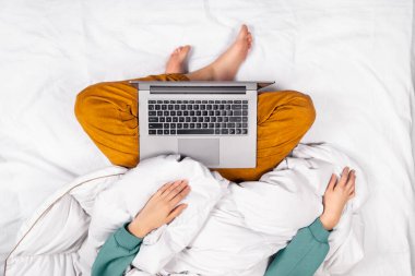 Evdeki yataktan modern dizüstü bilgisayarda çalışan kadınların üst görüntüsü. Ev ofisi ya da online eğitim konsepti. Laptop bir kadının kucağında. Üst görünüm pankartı.