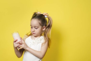 Küçük kız sarı arka planda izole edilmiş bir bardaktan yoğurt içiyor. Sağlıklı yeme kavramı.