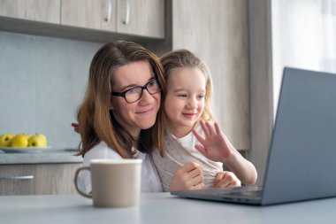 Anne ve kızı modern mutfakta oturup dizüstü bilgisayardan video izliyorlar. Ev Eğitimi kavramı.