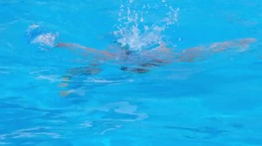 Kız havuza dalıyor ve suyun altında yüzüyor. Kız temiz mavi suyla havuza atlıyor ve yüzüyor. Yaz tatili kavramı. Yavaş çekim tam HD video