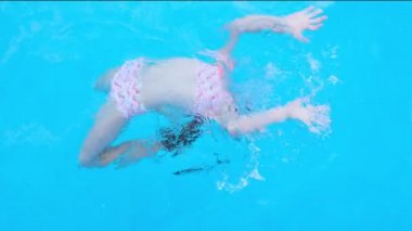 Kız takla atıyor ve şeffaf mavi yüzme havuzunda oynuyor. Çocuk yüzme havuzunda iyi eğlenceler. Tam HD yavaş çekim videosu