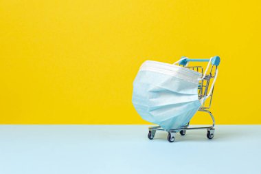 Coronavirus 'a karşı koruyucu tıbbi maskeli alışveriş arabası ya da tramvay. Karantina konseptiyle güvenli ve online alışveriş. Parlak sarı arkaplan, boşluğu kopyala.