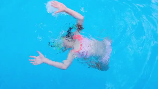 Дівчинка сортує і грає у прозорій блакитній воді басейну. Дитина розважається в басейні. Повне HD повільне відео руху — стокове відео