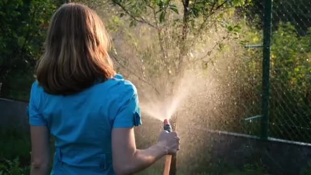 Młoda kobieta podlewa ogród w swoim letnim domu. Zajmij się koncepcją ogrodu. Strzelanie do słońca. — Wideo stockowe