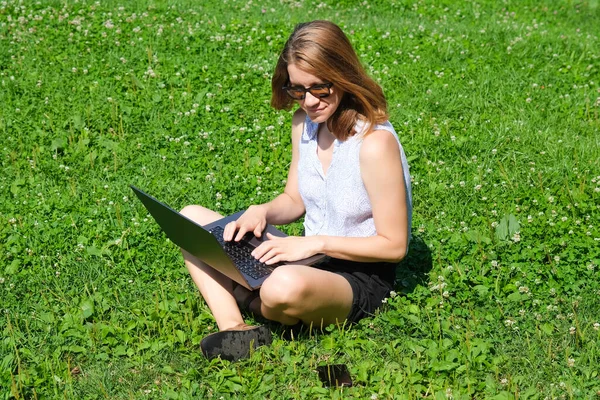 年轻的女孩或女人坐在公园的草地上，在笔记本电脑上工作。自由、教育或在线工作概念 — 图库照片