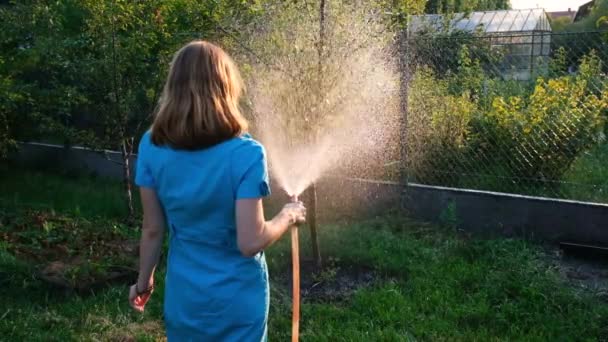 Eine junge Frau gießt den Garten an ihrem Sommerhaus. Achten Sie auf das Gartenkonzept. Schießen gegen die Sonne. Zeitlupe Full-HD-Video — Stockvideo