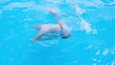 Kız takla atıyor ve şeffaf mavi yüzme havuzunda oynuyor. Çocuk yüzme havuzunda iyi eğlenceler. Tam HD yavaş çekim videosu