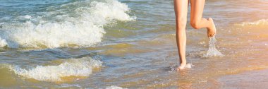 Deniz sahilinde koşan kız bacakları. Fotokopi alanı olan uzun bir yaz afişi. Sahilde yürüyen ya da koşan genç bir kızın bacaklarını dalgalar ve deniz köpüğüyle kapatın.