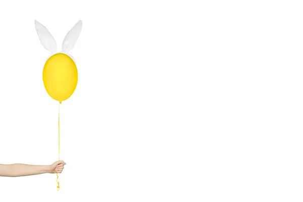 Concept minimaliste créatif de Pâques. Main tenant un ballon jaune dans les oreilles de lapin isolé sur blanc. Bannière monochrome avec espace de copie. — Photo