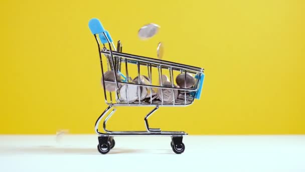 硬币落在玩具超市购物车或推车上，与明亮的黄色背景隔离。网上购物或销售安全概念. — 图库视频影像