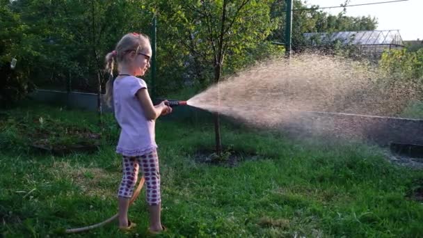 Bambine che annaffiano il giardino della sua casa estiva. Prenditi cura del concetto di giardino. Sparare contro il sole. Video Full HD al rallentatore. — Video Stock