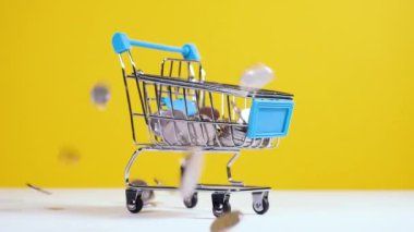 Paralar oyuncak süpermarket arabasına ya da parlak sarı arka planda izole edilmiş tramvaya düşer. Güvenli online alışveriş ya da satış konsepti. Tam HD yavaş çekim videosu